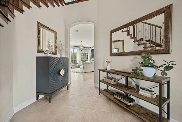 corridor with baseboards, a chandelier, stairs, light tile patterned floors, and arched walkways