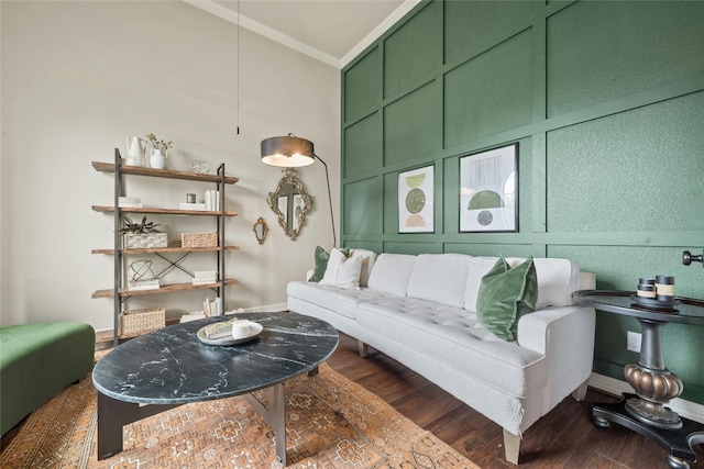 living area featuring crown molding, a decorative wall, and dark wood finished floors