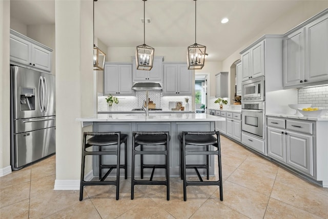 kitchen with under cabinet range hood, light countertops, appliances with stainless steel finishes, light tile patterned floors, and gray cabinetry