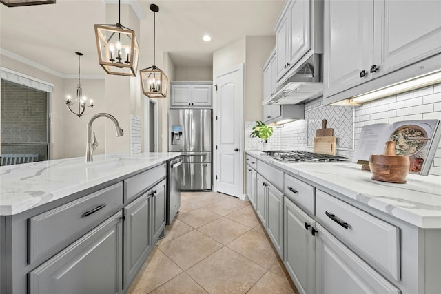 kitchen with under cabinet range hood, appliances with stainless steel finishes, an island with sink, decorative light fixtures, and a sink