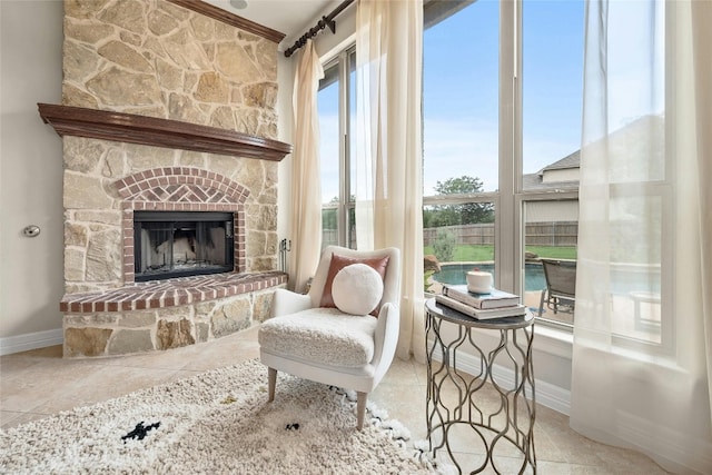 living area featuring baseboards, a stone fireplace, and light tile patterned floors