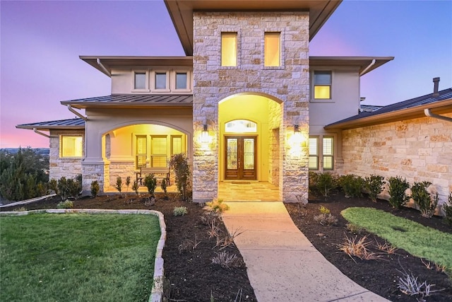 exterior entry at dusk with french doors, metal roof, a standing seam roof, a yard, and stucco siding