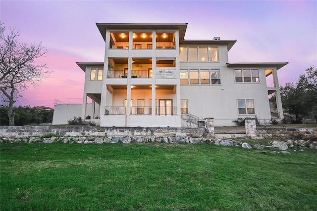 205 Palazza Alto Dr, Austin, TX 78734 - back of house at dusk with a balcony, a lawn, and stucco siding