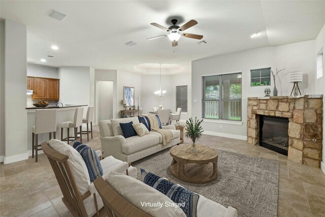 living room with a stone fireplace, ceiling fan with notable chandelier, baseboards, and visible vents