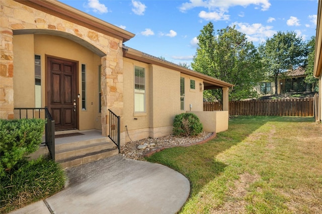 entrance to property featuring fence, stucco siding, and a yard