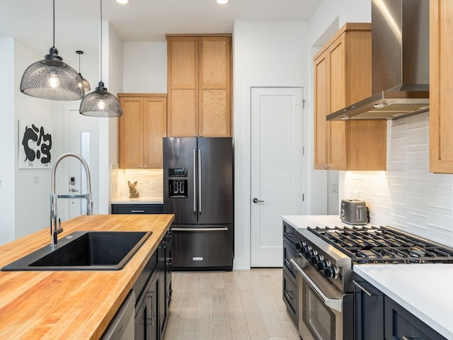 kitchen featuring wall chimney range hood, premium appliances, wood counters, pendant lighting, and sink