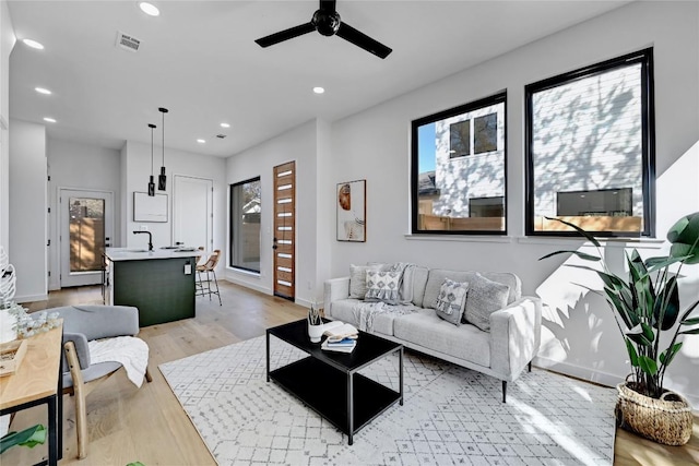 living room with ceiling fan, light wood-type flooring, and sink