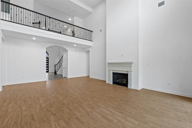 2324 Bel Paese Bnd, Leander, TX 78641 - unfurnished living room featuring wood finished floors, stairs, a towering ceiling, a glass covered fireplace, and arched walkways