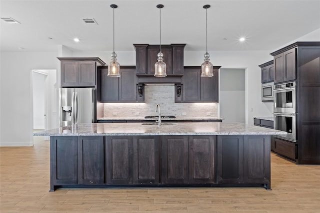 2324 Bel Paese Bnd, Leander, TX 78641 - kitchen featuring appliances with stainless steel finishes, a large island with sink, backsplash, light wood-type flooring, and recessed lighting