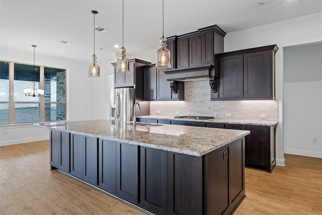 2324 Bel Paese Bnd, Leander, TX 78641 - kitchen featuring appliances with stainless steel finishes, backsplash, light wood finished floors, an island with sink, and exhaust hood