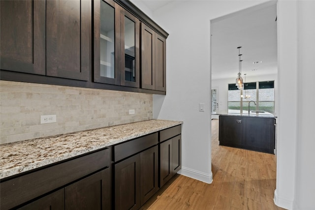 2324 Bel Paese Bnd, Leander, TX 78641 - kitchen with dark brown cabinetry, light wood-style flooring, decorative backsplash, glass insert cabinets, and light stone counters