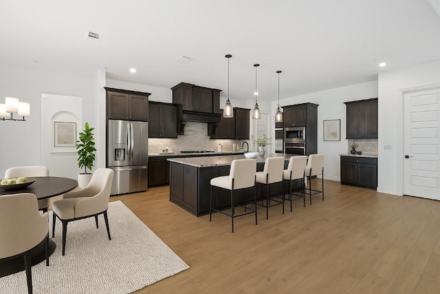 2324 Bel Paese Bnd, Leander, TX 78641 - kitchen with appliances with stainless steel finishes, decorative backsplash, dark brown cabinets, light wood-style floors, and a breakfast bar