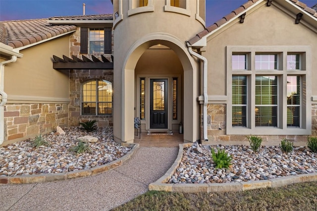 exterior entry at dusk with a tiled roof, stucco siding, and stone siding