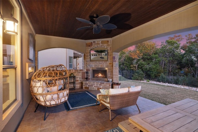 patio terrace at dusk featuring an outdoor stone fireplace, fence, and a ceiling fan