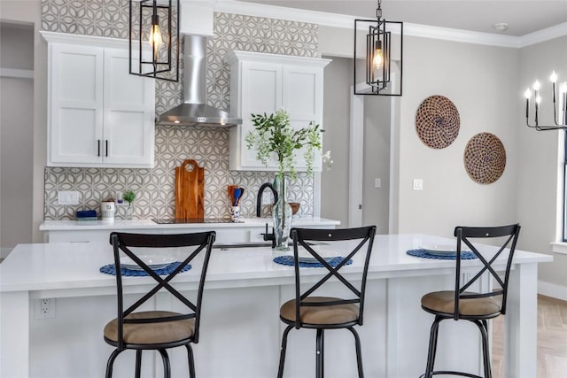 kitchen with a breakfast bar area, wall chimney range hood, light countertops, ornamental molding, and white cabinets