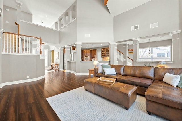 living area with wood finished floors, visible vents, baseboards, decorative columns, and stairs