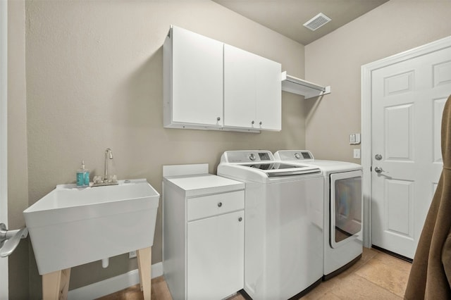 washroom with a sink, visible vents, separate washer and dryer, and cabinet space