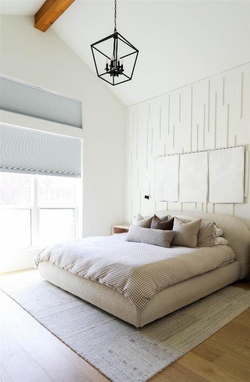 bedroom featuring an inviting chandelier, beam ceiling, high vaulted ceiling, and wood finished floors