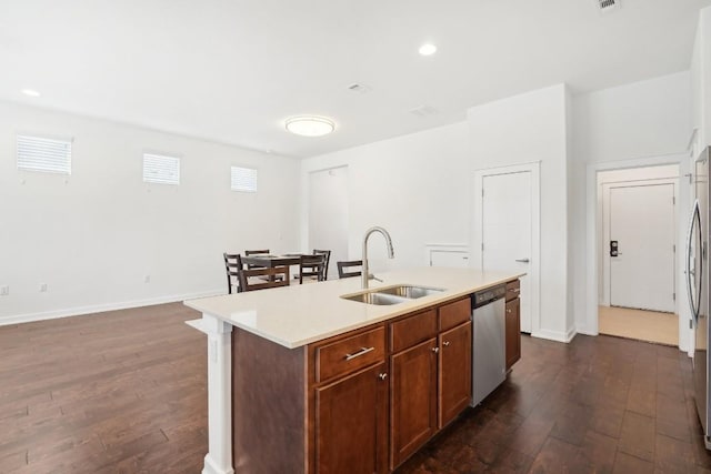 kitchen with a sink, light countertops, stainless steel dishwasher, an island with sink, and dark wood finished floors