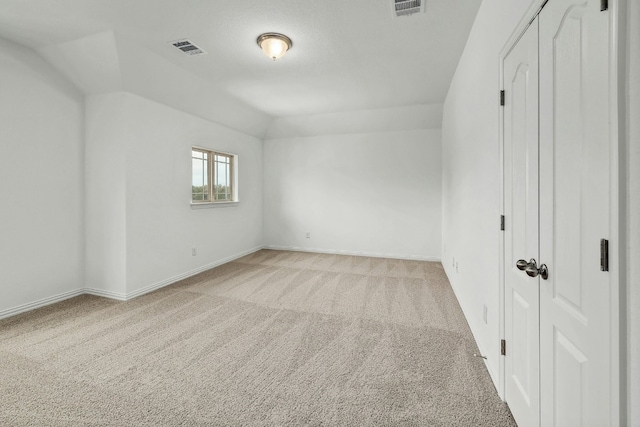 empty room featuring vaulted ceiling, visible vents, light carpet, and baseboards