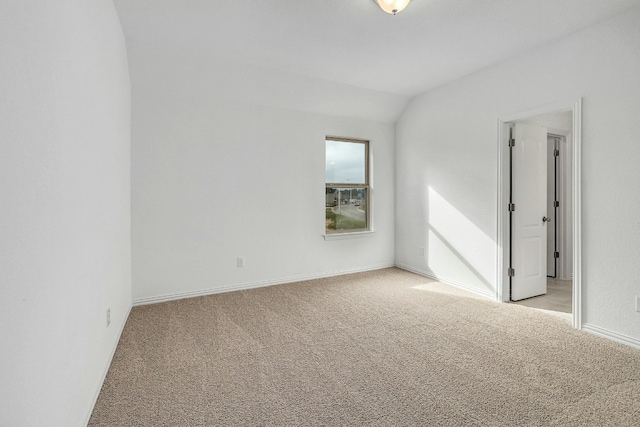 unfurnished room featuring baseboards, lofted ceiling, and light carpet