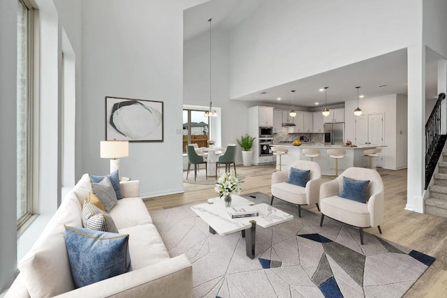 living area featuring stairs, baseboards, a high ceiling, light wood-type flooring, and a notable chandelier