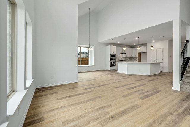 unfurnished living room featuring baseboards, a chandelier, light wood-type flooring, stairs, and a high ceiling