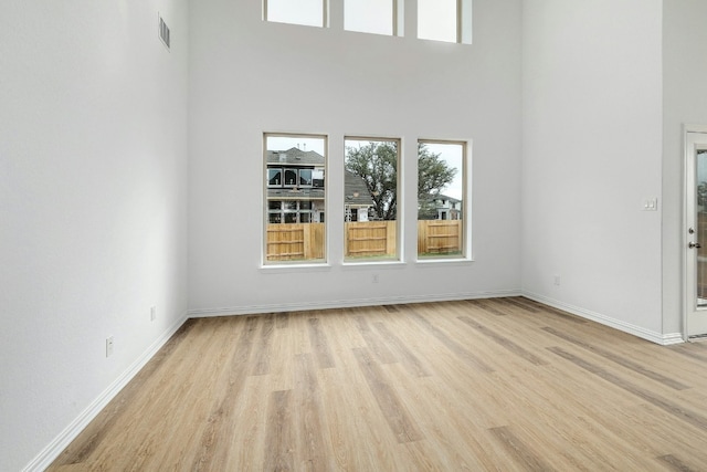 interior space with baseboards, light wood finished floors, visible vents, and a high ceiling