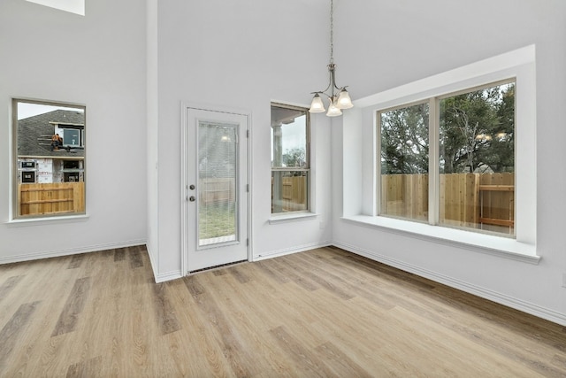 unfurnished dining area featuring baseboards, a healthy amount of sunlight, light wood finished floors, and a chandelier