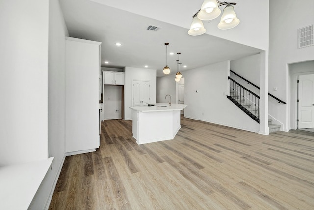 kitchen with hanging light fixtures, visible vents, light countertops, white cabinetry, and an island with sink