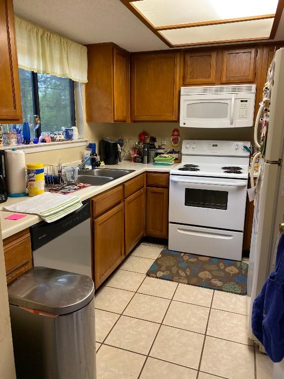 kitchen with a sink, brown cabinetry, light countertops, and white appliances