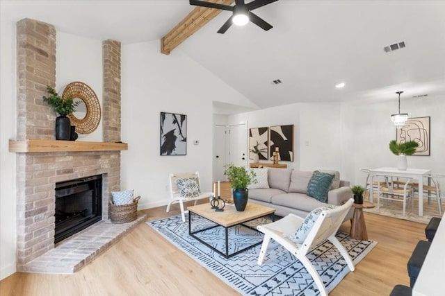 living room featuring lofted ceiling with beams, a fireplace, wood finished floors, and visible vents