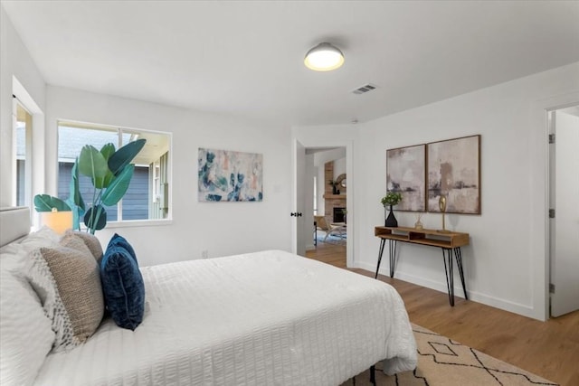 bedroom featuring baseboards, a fireplace, visible vents, and wood finished floors