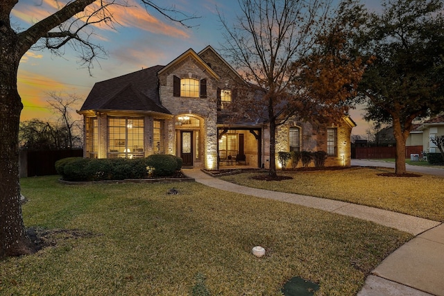 french provincial home featuring fence, stone siding, and a front yard