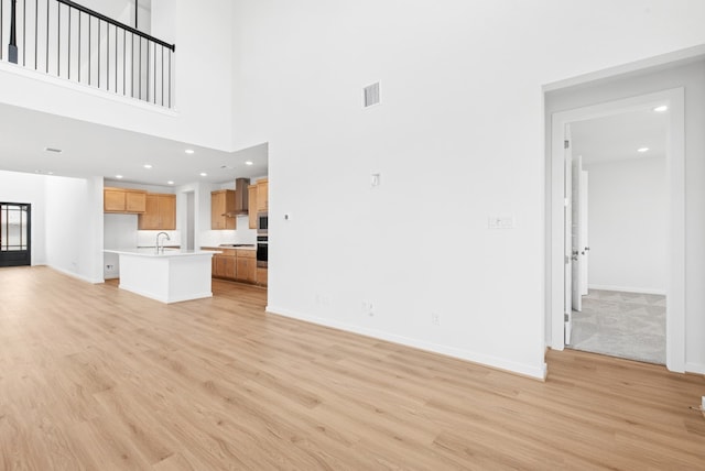 512 Palatino Bnd, Liberty Hill, TX 78642 - unfurnished living room featuring a sink, light wood-type flooring, baseboards, recessed lighting, and a towering ceiling