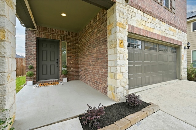 doorway to property with a garage, concrete driveway, and brick siding