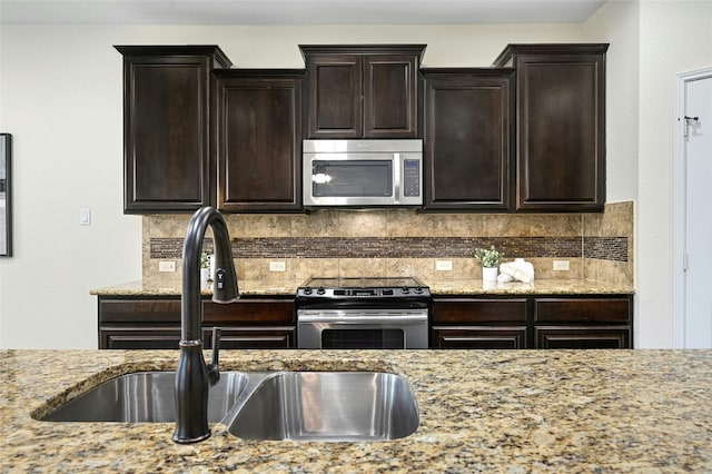 kitchen featuring dark brown cabinetry, stainless steel appliances, a sink, backsplash, and light stone countertops