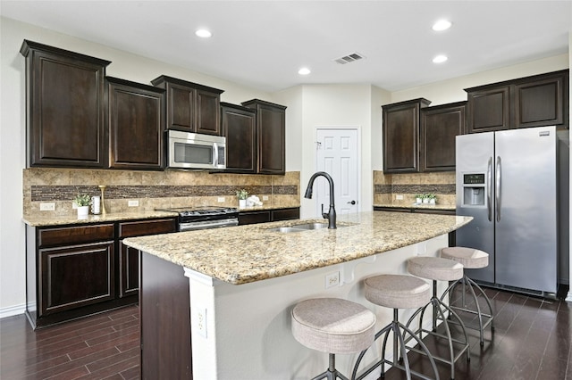 kitchen with visible vents, dark wood-style floors, a kitchen island with sink, stainless steel appliances, and a sink