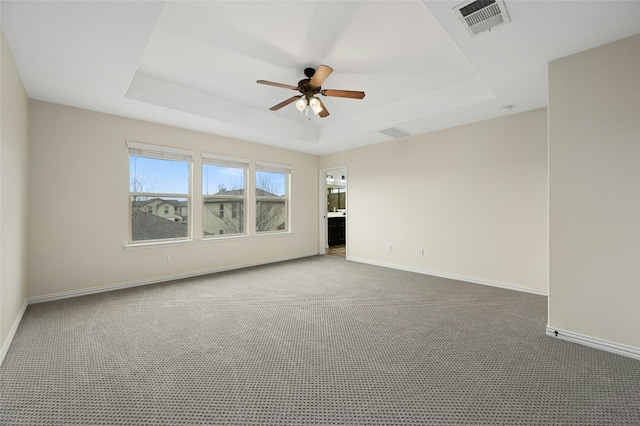 carpeted empty room featuring ceiling fan, a raised ceiling, visible vents, and baseboards