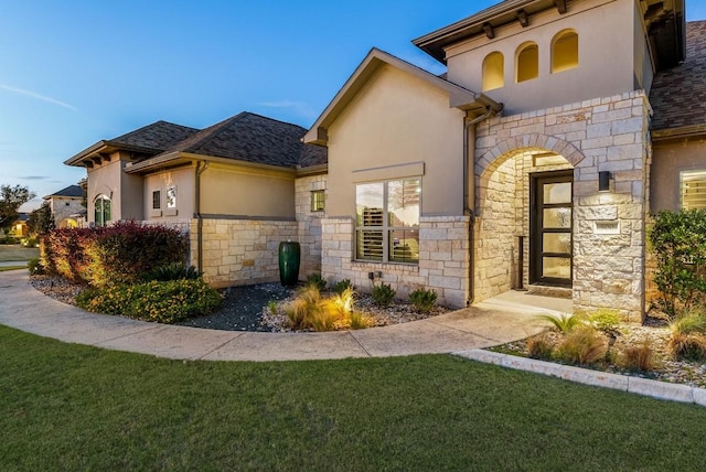 view of front facade with stone siding, a front lawn, and stucco siding