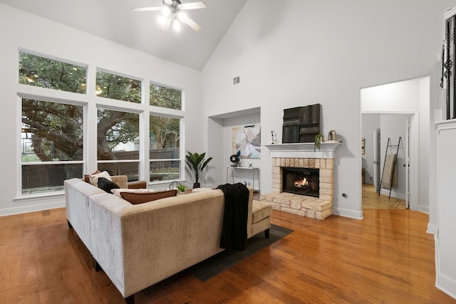 living area featuring high vaulted ceiling, a brick fireplace, baseboards, and wood finished floors