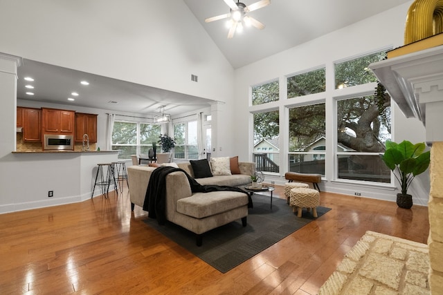 living area featuring ceiling fan, high vaulted ceiling, recessed lighting, light wood-style floors, and ornate columns