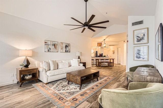 living area featuring light wood finished floors, baseboards, visible vents, lofted ceiling, and ceiling fan with notable chandelier