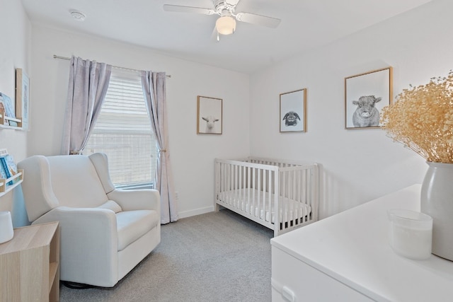 bedroom featuring light colored carpet, a nursery area, a ceiling fan, and baseboards