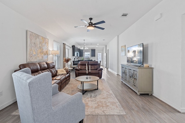 living area featuring ceiling fan with notable chandelier, light wood finished floors, visible vents, and baseboards