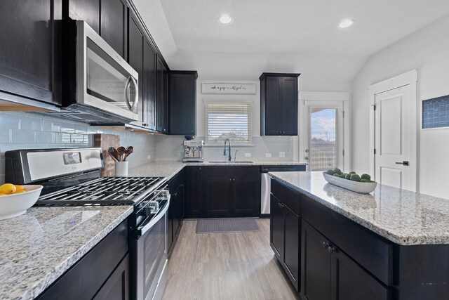 kitchen with appliances with stainless steel finishes, dark cabinets, a sink, light wood-style flooring, and recessed lighting