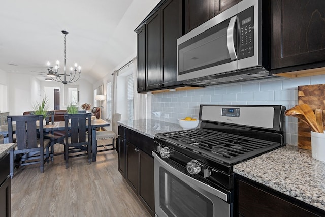 kitchen with stainless steel appliances, a chandelier, vaulted ceiling, decorative backsplash, and light wood-style floors