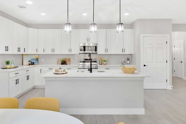 137 Puu Waa Waa Ln, Bastrop, TX 78602 - kitchen featuring stainless steel microwave, an island with sink, tasteful backsplash, white cabinetry, and recessed lighting