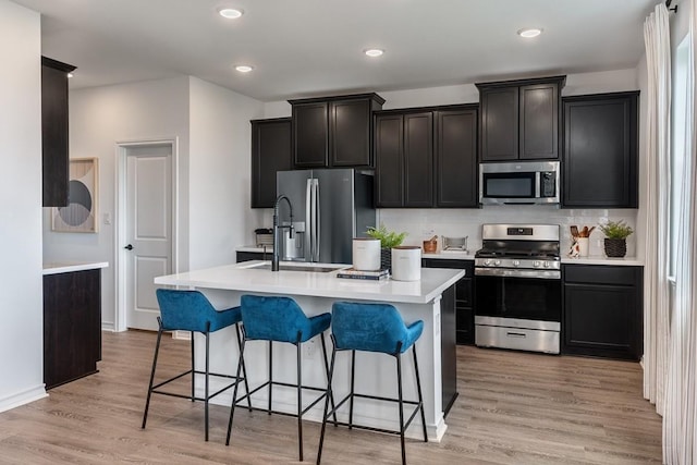 kitchen with stainless steel appliances, light wood-style flooring, light countertops, and a center island with sink