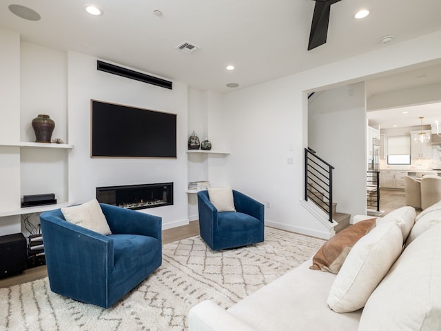 living room with stairs, a glass covered fireplace, visible vents, and recessed lighting